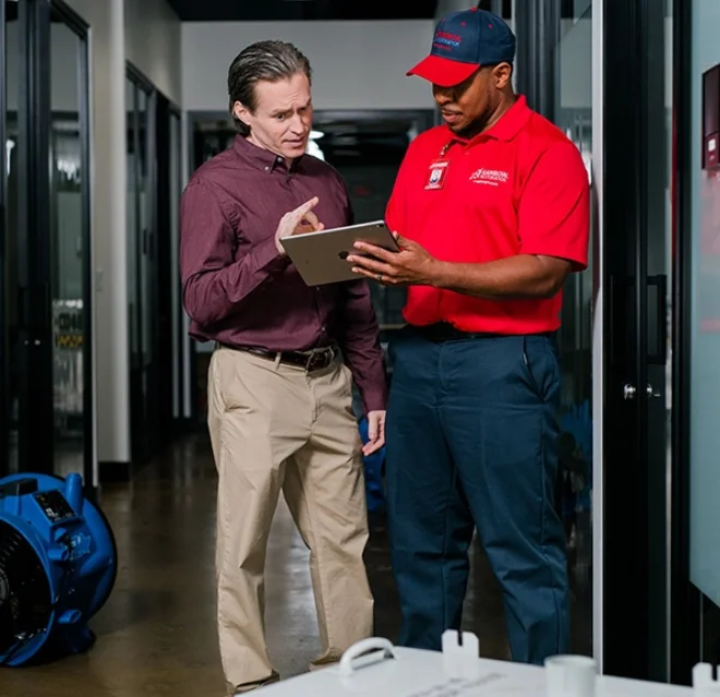A Rainbow Restoration service professional and a business customer reviewing a restoration plan on a tablet next to a high-powered fan.