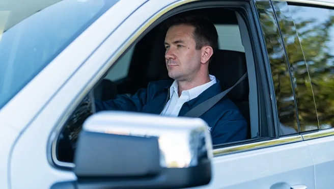 A Rainbow Restoration service professional in the driver's seat of a car, arriving at a job site in need of full-service reconstruction.
