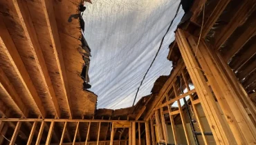 Emergency roof tarping covers a storm-damaged home in Jonesborough with exposed framing and roof decking visible inside.