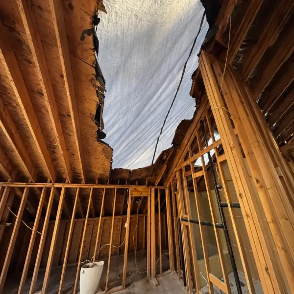 Emergency roof tarping covers a storm-damaged home in Jonesborough with exposed framing and roof decking visible inside.
