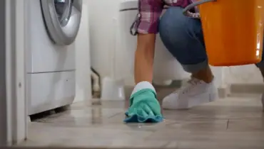 Woman wearing rubber gloves cleaning up water that is leaking from a washing machine.