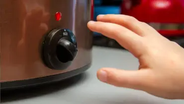 Child’s hand reaching for the dial on a slow cooker.